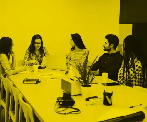 A group of 4 women and one man sitting around a meeting table at the office in discussion with each other.