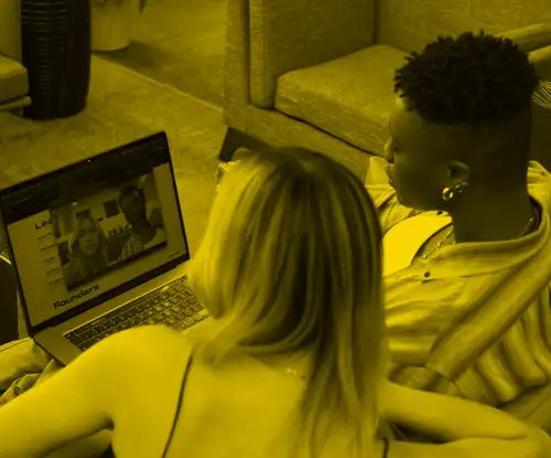 A non-binary person and transfeminine person on a video call in an office