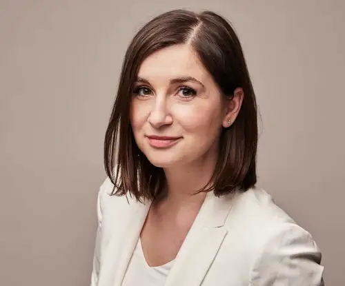 Portrait of a woman in a white suit standing in front of a plain beige back drop