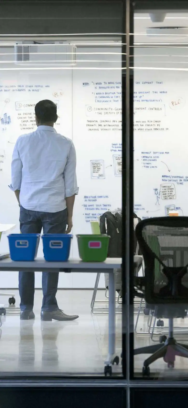 One student looks at a white board while his group members do other work in the room.