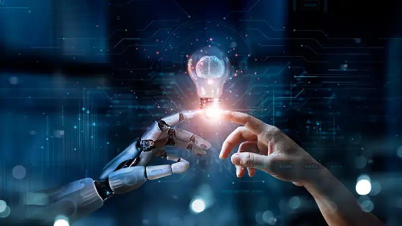 A robotic hand and human hand touching fingers with a lightbulb emerging from their connection