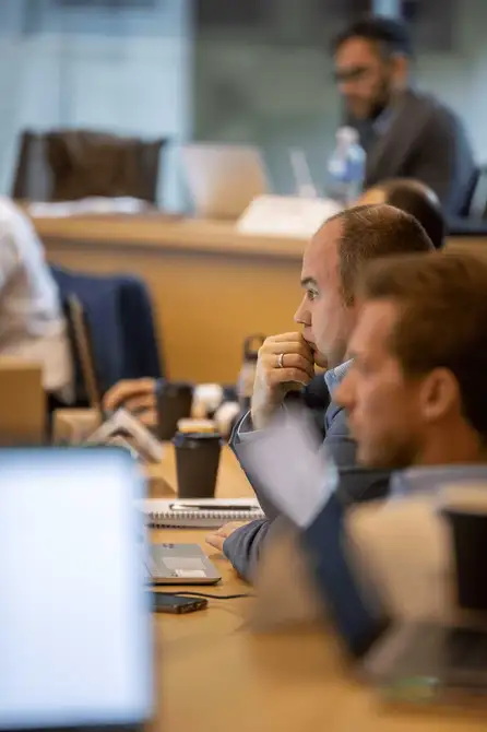 A row of people listens to a speaker off screen.