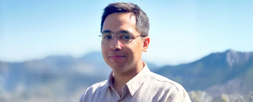 A smiling man standing infront of a mountain range