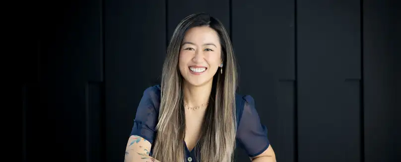 A smiling woman wearing a blue shirt sits in front of a series of black lockers